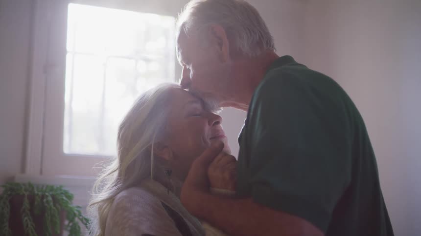 Elderly man with a shirt kisses elderly womans forehead with love and affection