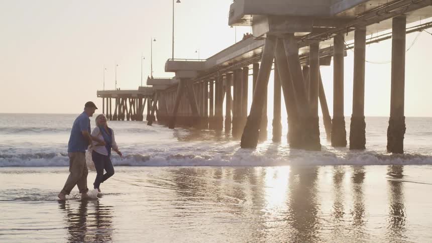 An elderly couple walking together in water on a beach