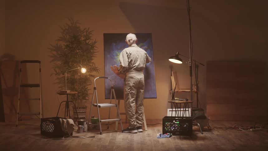 A painter walks toward a large canvas while holding a paint palette to finish his artwork