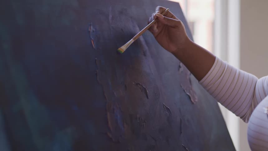 An artist applies blue brushstrokes to a canvas