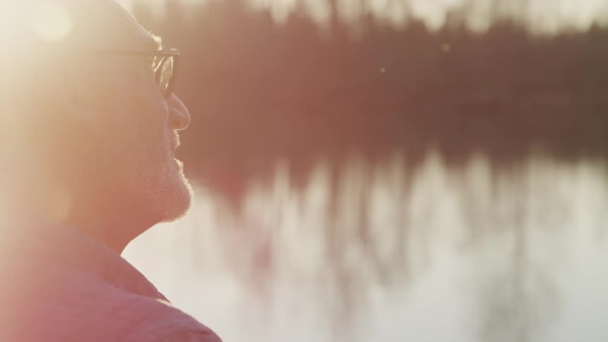 Man stands on shore of lake that reflects woods on opposite shore