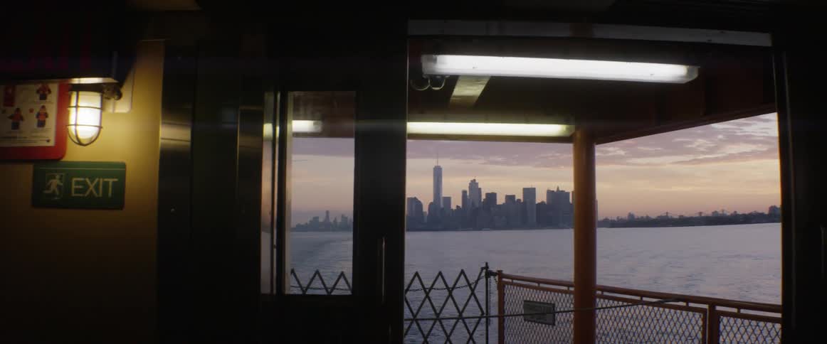 A boat floats away from a cityscape at sunset
