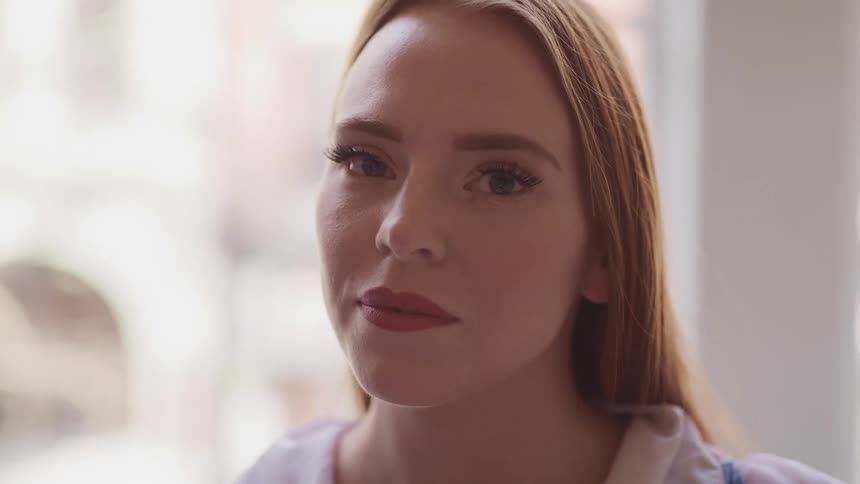 Young blonde woman in a room turns around to look at the camera