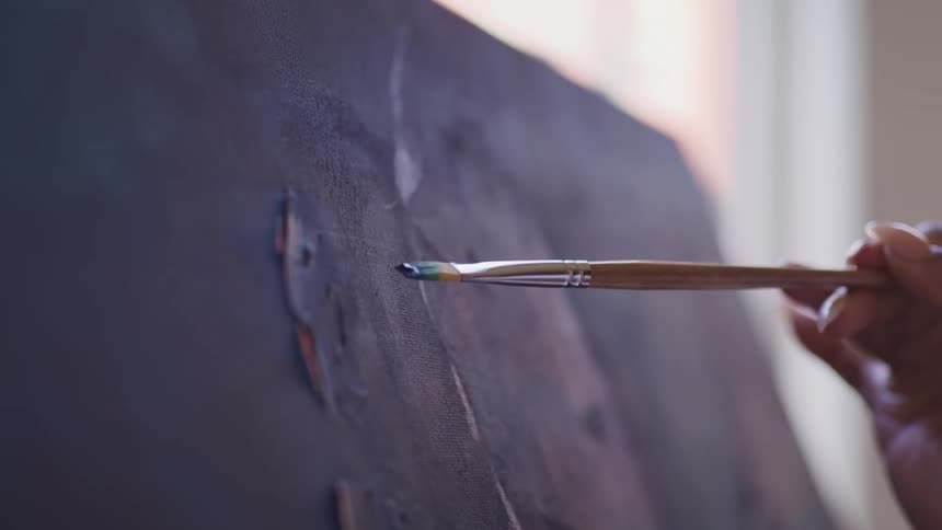 A woman uses a paint brush to brush strokes on a large canvas