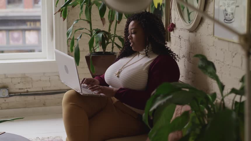 A woman is sitting indoors and typing on a laptop