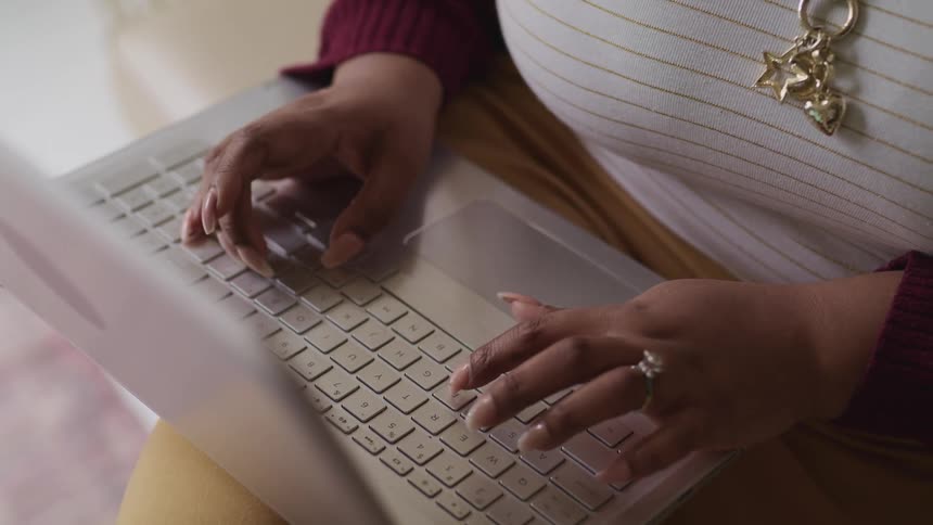 A woman typing on a laptop that is on her knee