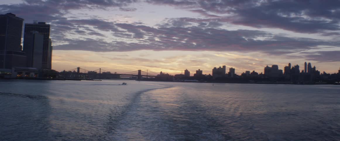 A boat travelling through an urban harbor at sunset