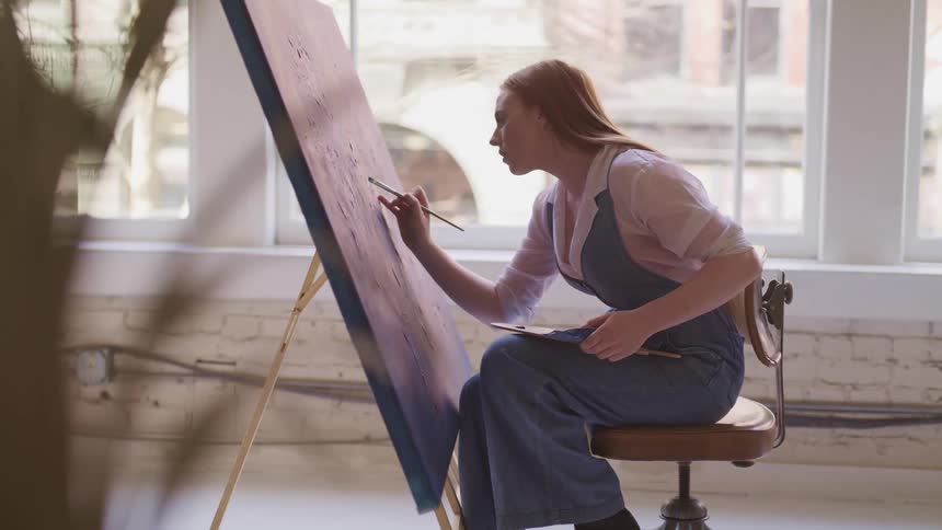 Woman sitting in a chair painting on canvas with a brush in a studio