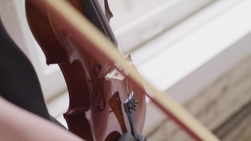 A person holding a violin and a bow with a window in the background