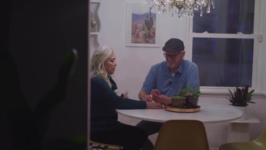 Elderly man and woman sitting at a table play cards in a room