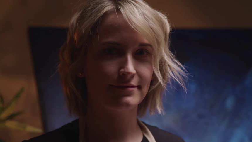 A woman is standing indoors and smiling