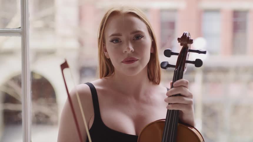 A woman with a violin next to a window with buildings in the background