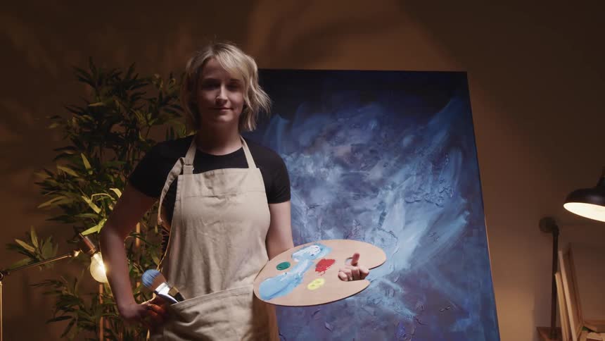 An artist holding a palette poses in front of her work