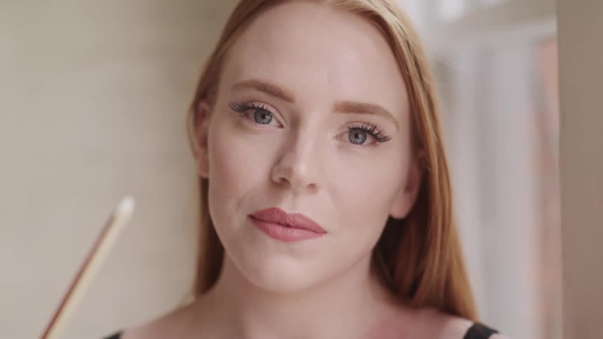 Woman with blue eyes and red hair faces the camera with eye contact