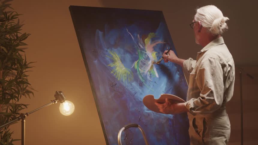 An elderly man is painting on a canvas