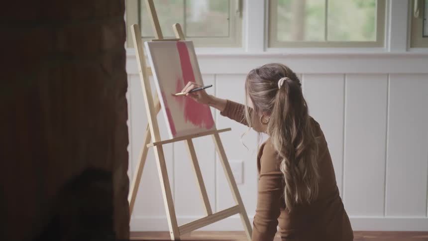 A woman paints on a canvas while sitting on a floor