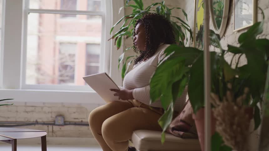 A woman sitting on a couch next to a table with a window in the background