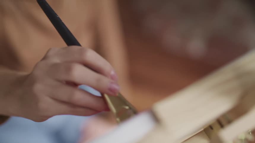 A person sitting in front of a canvas holding a paint brush and painting