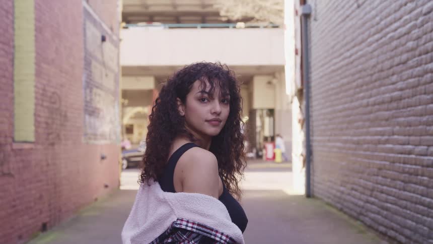 Woman with curly hair looks over her shoulder in an alley