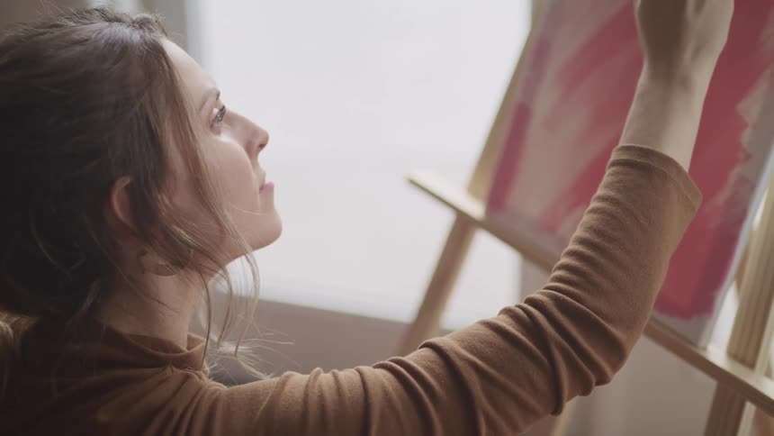 A woman uses a paintbrush to paint red strokes on a canvas