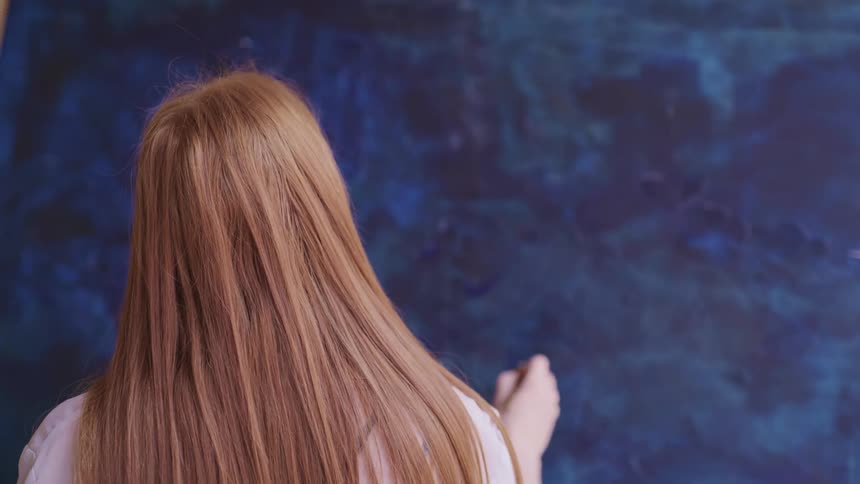 A woman paints on a large canvas with a small paint brush