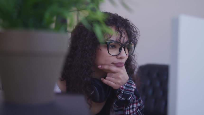 Woman sits contemplating monitor with headphones hanging around her neck