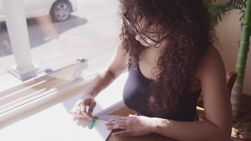 A woman sitting inside a building beside a window sketches