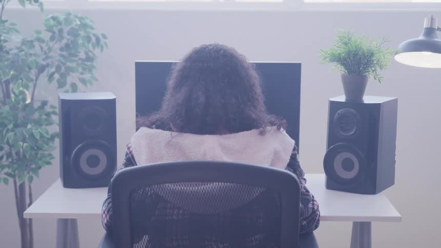 Woman with curly hair sits at a table and uses a computer with speakers