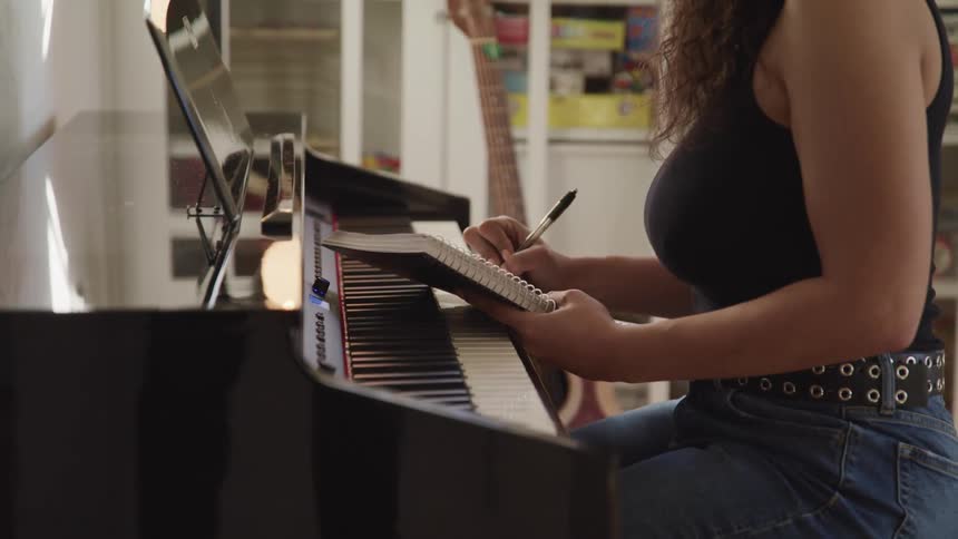 A woman sitting at a keyboard writes in a notebook