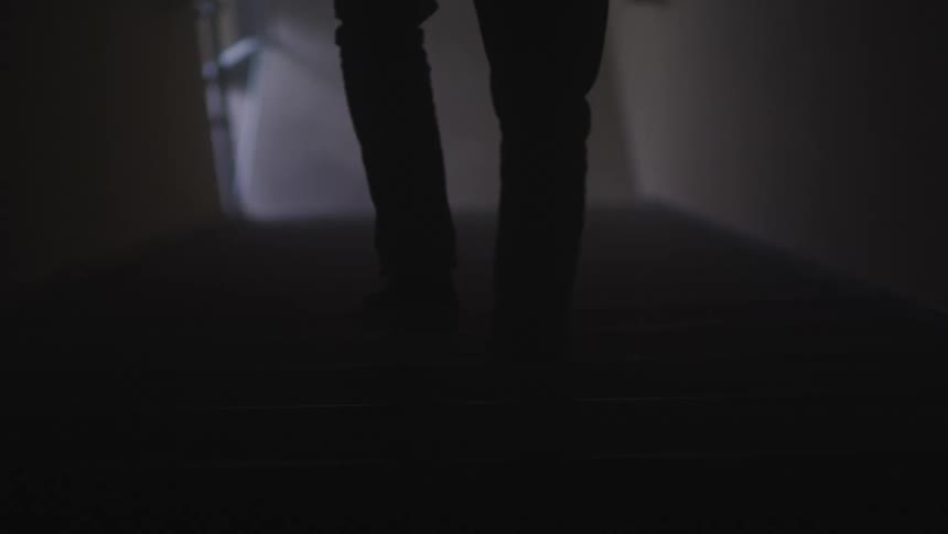 A man slowly descends down a set of stairs in the darkness