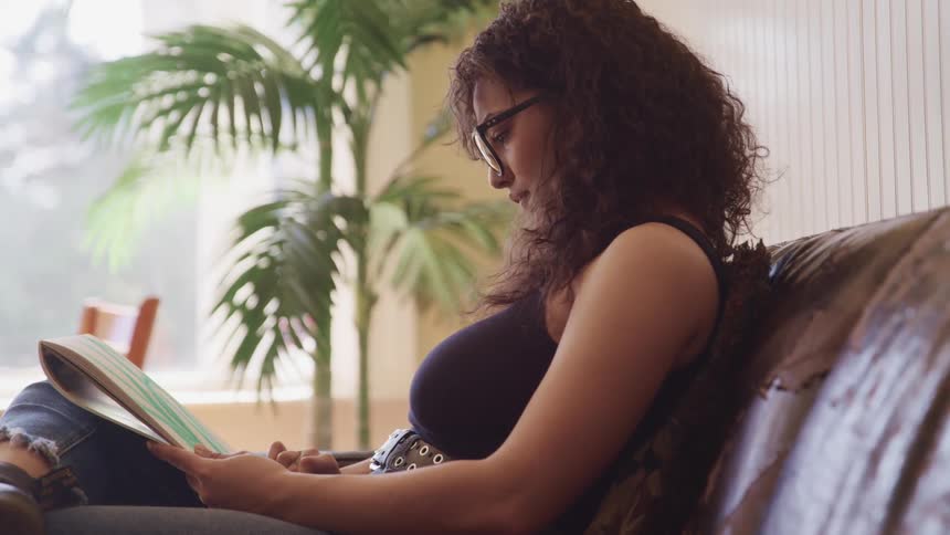 Young woman wearing glasses draws on paper with green chalk while sitting in a couch