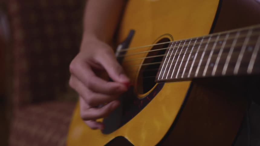 Close up of a hand playing a guitar by pulling the strings with his fingers