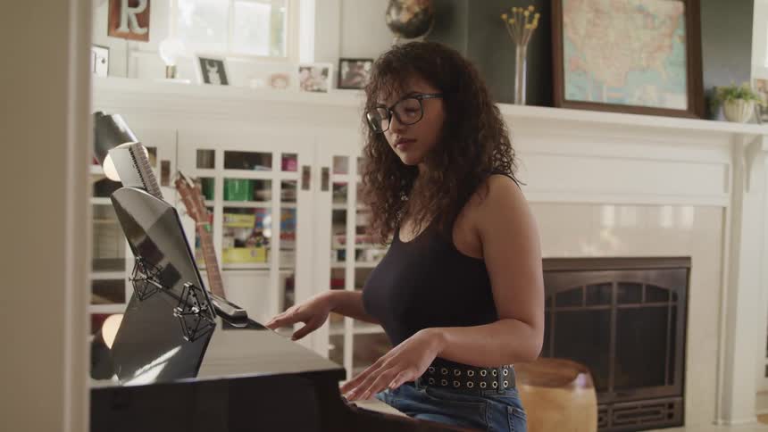 Woman with glasses and curly hair plays a grand piano by pressing the black and white keys on the keyboard