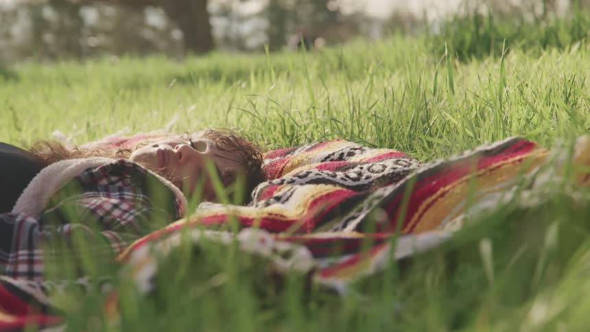 A woman laying on a blanket on a grassy field with trees and the sky in the background