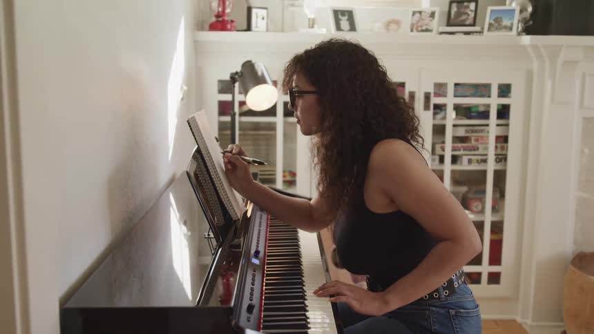 Young woman sitting in a piano in the living room writes musical notation