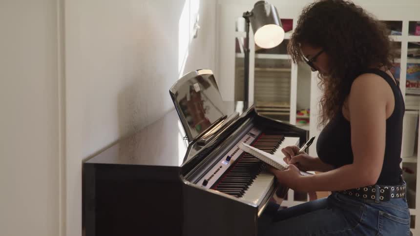 A woman is sitting at the piano writing notes