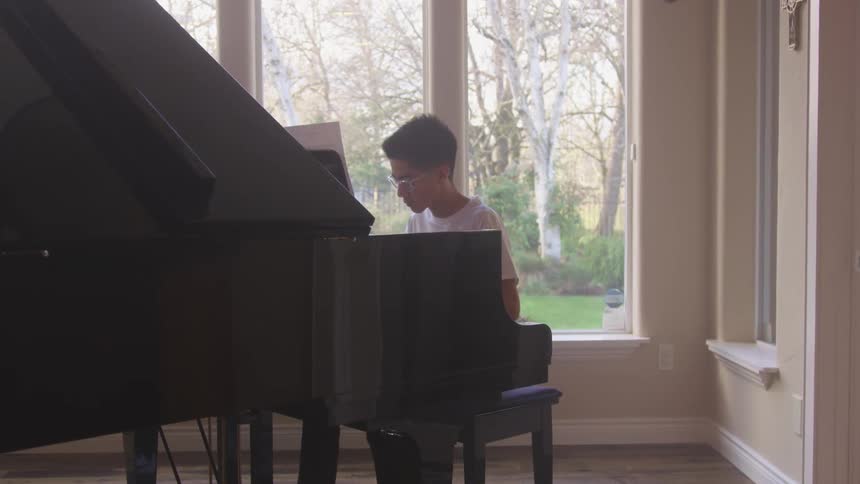 A young man sits at a grand piano and plays a song with a lot of movement of his head
