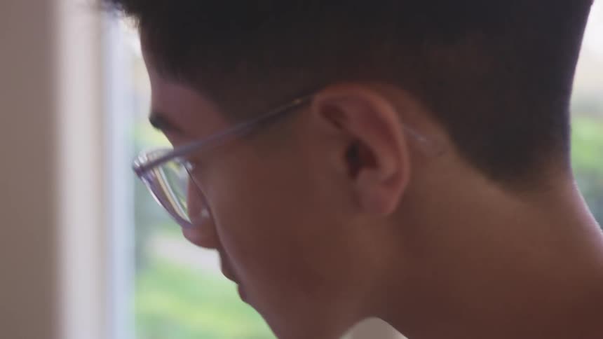 Side view of a teenage boy playing the piano in a room