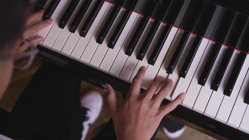 A young man wearing eyeglasses plays the piano