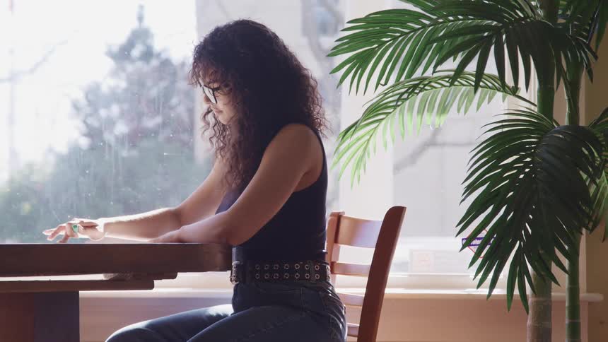 A woman is sitting at the table by the window