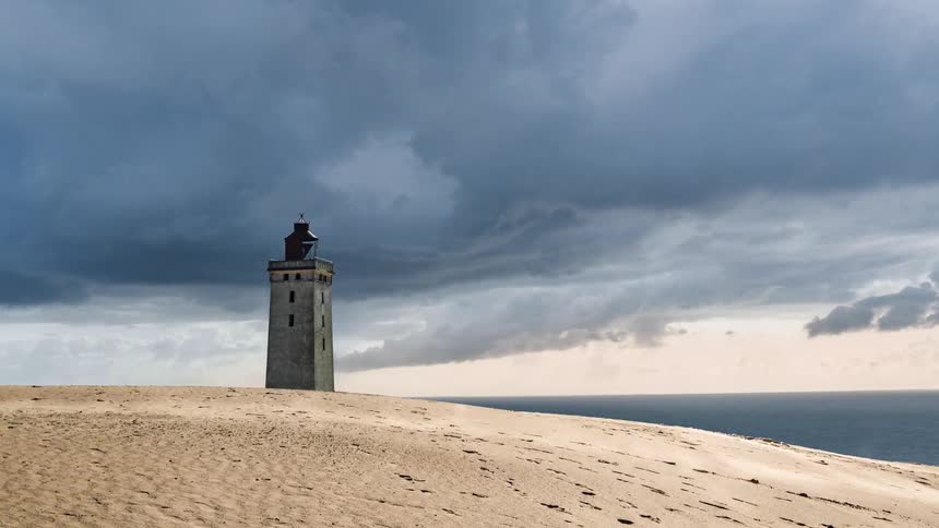Clouds flow over the lighthouse by the water
