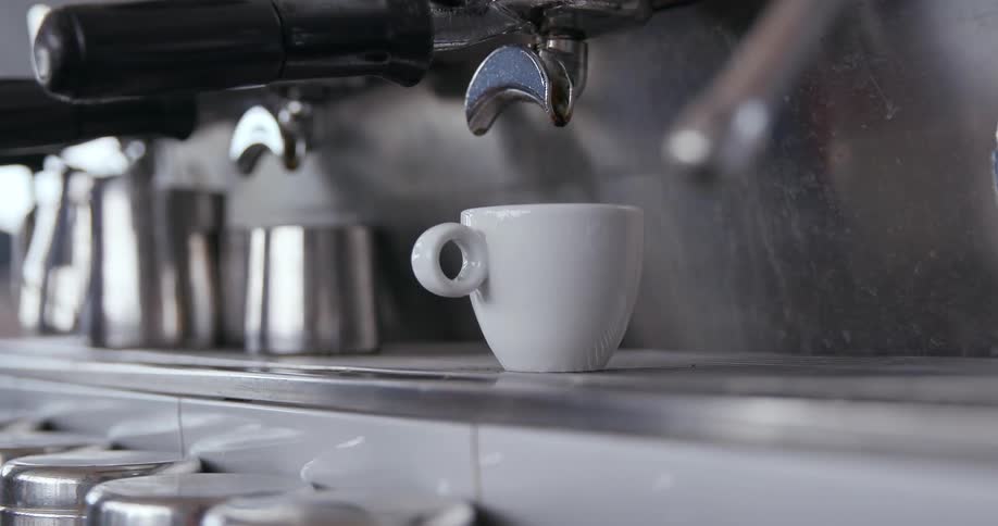 A man in a cafe picks up an espresso cup from under a machine