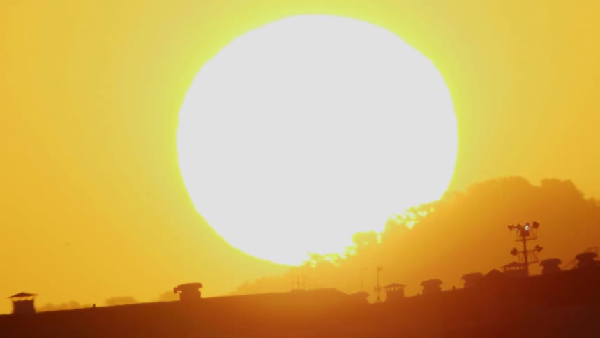 The sun shines brightly and turns the sky orange as it sets over a building