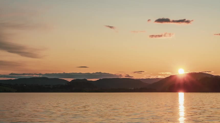 A lake with trees hills the sunset the sky and clouds in the background