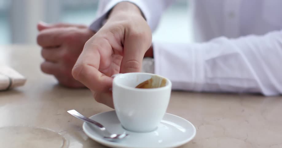 Man wearing a shirt places a cup of coffee over a dish after drinking it