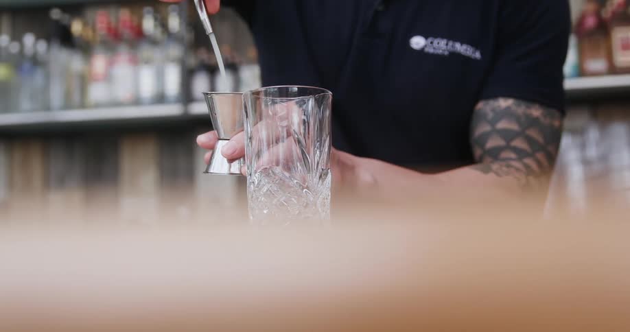 A bartender pours liquor into a jigger and then into a glass