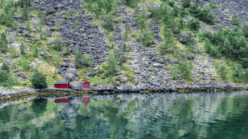 A cottage sits at the base of a hill on the shore