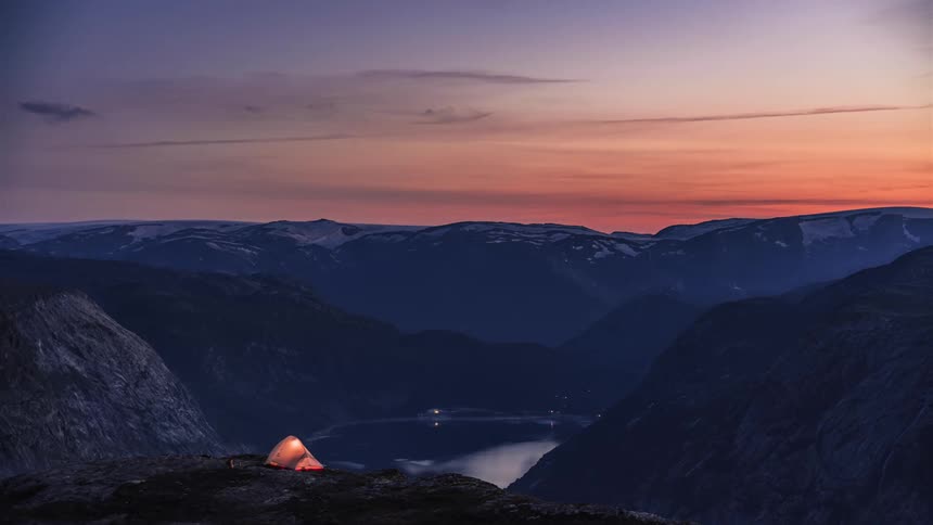 Clouds pass over a lake surrounded by mountains at sunset
