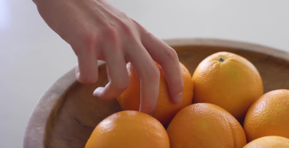 A woman grabs an orange out of a wooden bowl