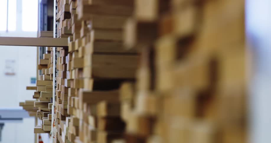 A hand pulls a piece of lumber from a stack in a warehouse